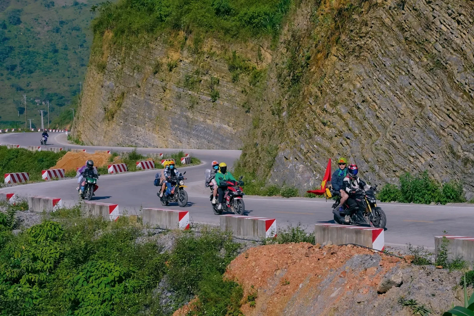 Motorbike riders with a Vietnamese flag wind along a mountain pass on the Ha Giang Loop.